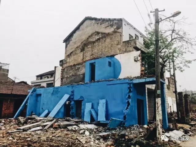 △ 這棟建筑是臨江最近的半拆遷建筑物的遺留，沅江和堤壩成為了展覽的天然背景。創(chuàng)作團(tuán)隊(duì)對(duì)這棟建筑進(jìn)行了半涂裝，將符號(hào)性的沅水曲線與拆遷進(jìn)行中的建筑立面進(jìn)行意義的疊造，它們共同觸發(fā)了場(chǎng)所空間多元語境的生成，把拆遷這種暫時(shí)破壞性、干擾性的介入行動(dòng)與沅水右岸發(fā)展的未來性、美好性緊密融合。
